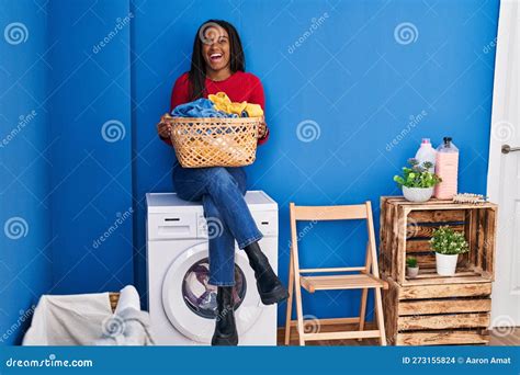 Young African American with Braids Holding Laundry Basket Sitting on Washing Machine Smiling and ...