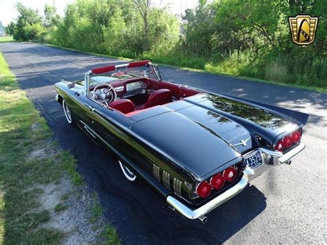 an old black convertible car parked on the side of the road in front of some trees