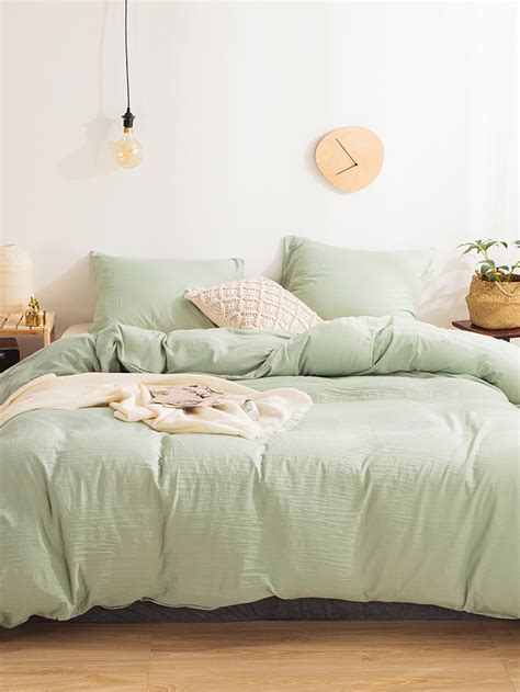 a bed with green sheets and pillows in a white room next to a wooden floor