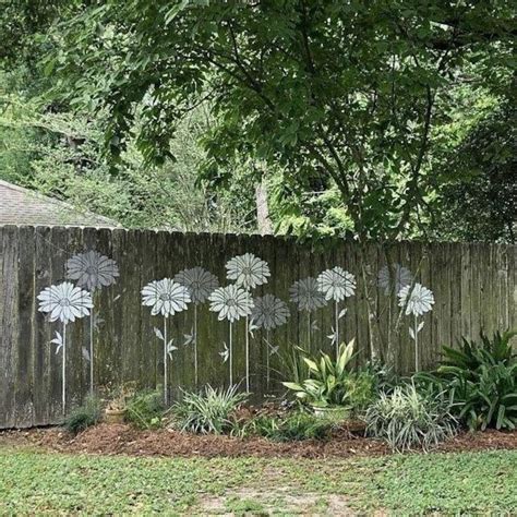 a fence with flowers painted on it next to grass and trees in the back yard