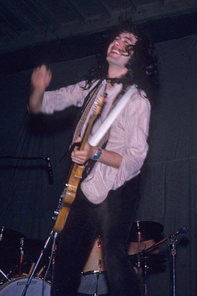 a man with long hair holding a guitar in his right hand and smiling at the camera