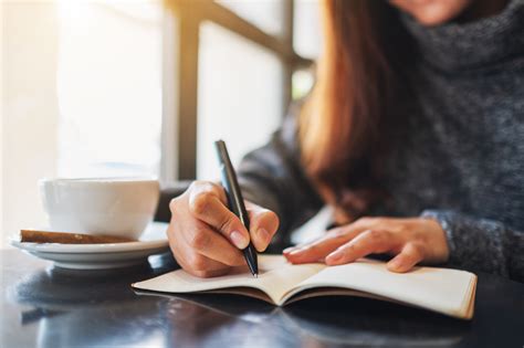 Closeup image of a woman writing on a blank notebook on the table | Sunday Writers' Club