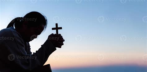 Silhouette of woman kneeling down praying for worship God at sky background. Christians pray to ...