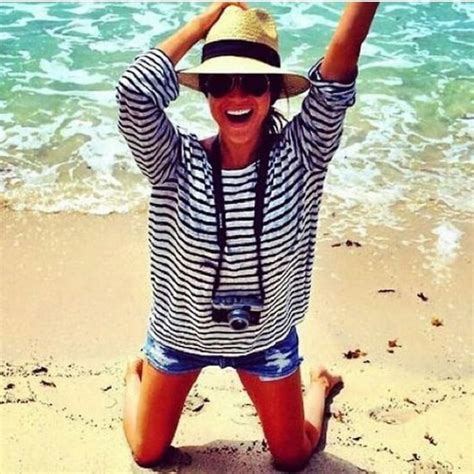 a woman sitting on top of a sandy beach next to the ocean wearing a hat