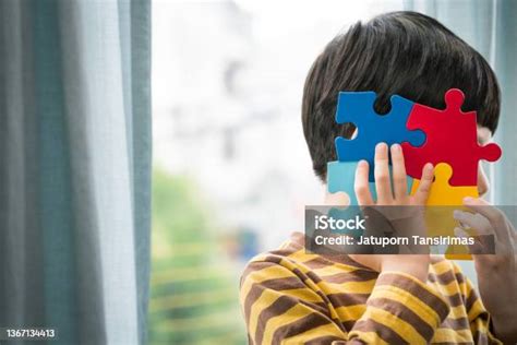 Autistic Asian Boy Holding Colorful Jigsaw Puzzle Covering His Face In His Room By Window As ...