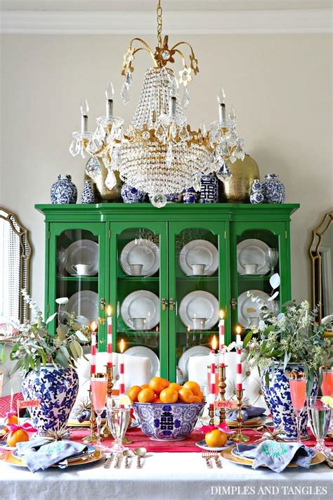 a dining room table with plates, cups and candles in front of a green china cabinet