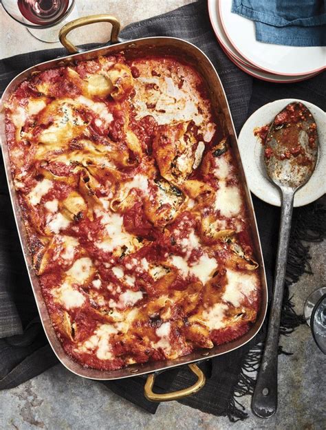 a casserole dish with meat and cheese on it next to two wine glasses