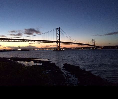 a bridge that is over some water at sunset or dawn with the sun setting behind it