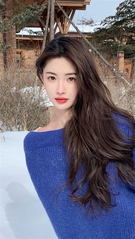 a woman with long brown hair standing in the snow wearing a blue sweater and red lipstick