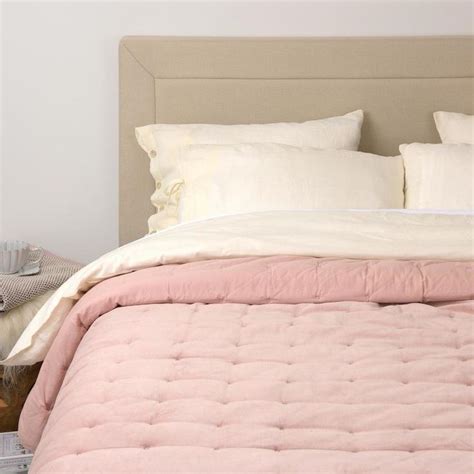 a bed with pink comforter and pillows on top of it next to a night stand