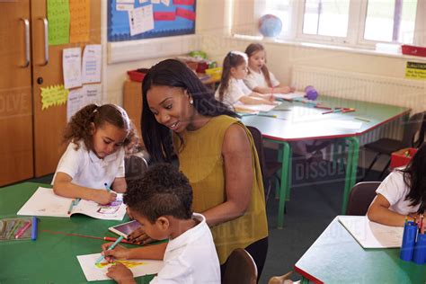 Female elementary school teacher helping pupils at desk - Stock Photo - Dissolve