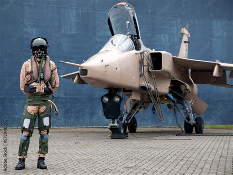 Fighter pilot standing with Military fighter Jet wearing flying helmet, suit and dark visor with ...