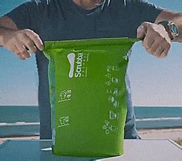 a man holding a green bag over a white table near the ocean and beach in front of him