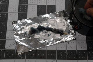 a person is holding something in their hand near a piece of tin foil on the floor