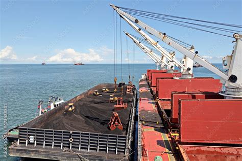 Loading coal from cargo barges onto a bulk carrier using ship cranes ...