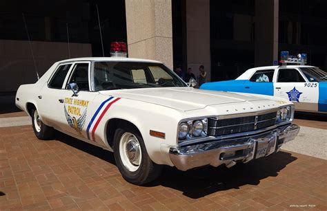 an old police car parked in front of a cop car on the side of the road