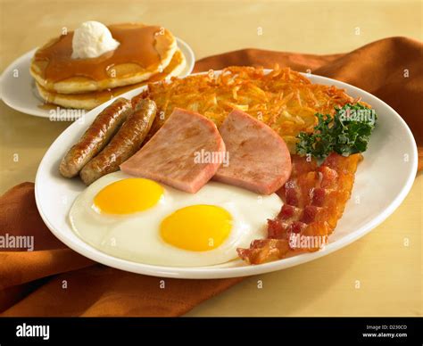 Egg sausage ham and bacon breakfast served with hash browns and pancakes Stock Photo - Alamy