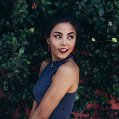 a woman standing in front of a bush with her hands on her hips and smiling at the camera