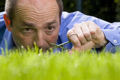 Germany, Baden-Württemberg, Stuttgart, Man cutting grass with scissors ...