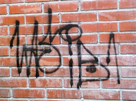 Picture of a single black graffiti tag, sprayed on a brick wall, in the sun-light of Spring, in ...