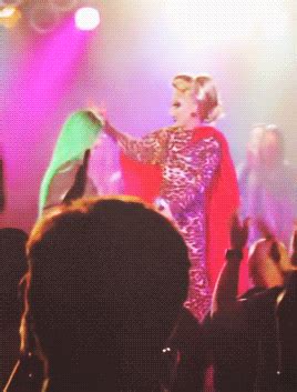 a woman in a costume standing on stage with her arms out to the side while people watch
