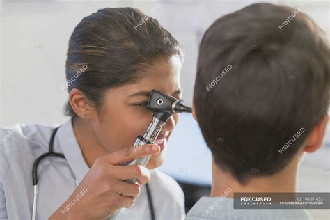 Female doctor using otoscope in ear of patient — medical exam, indian ...