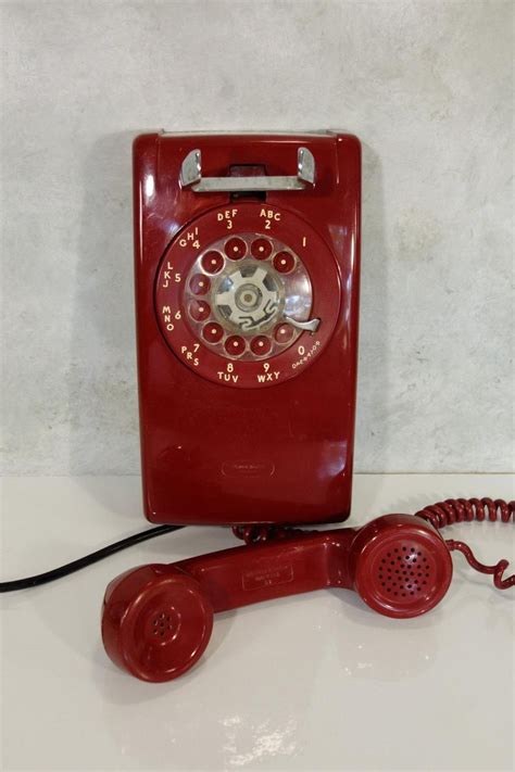 an old fashioned red phone sitting on top of a white counter next to a telephone cord