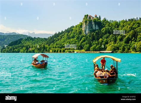 Tourists ride on traditional wooden pletna, Lake Bled, Slovenia, with Bled Castle behind and the ...