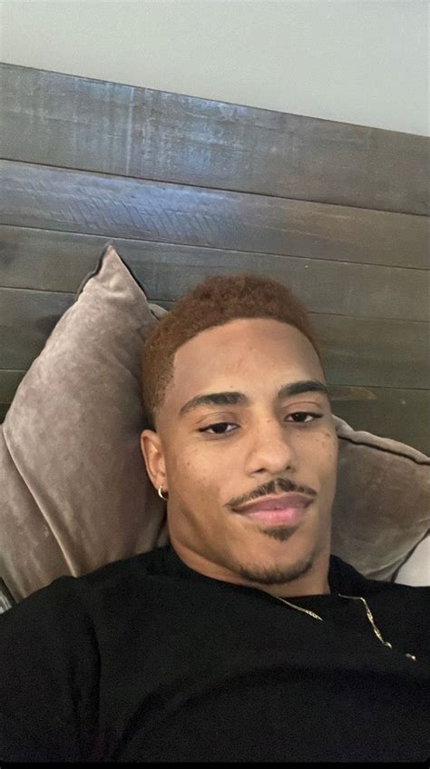 a man laying on top of a bed in a black shirt and silver earring