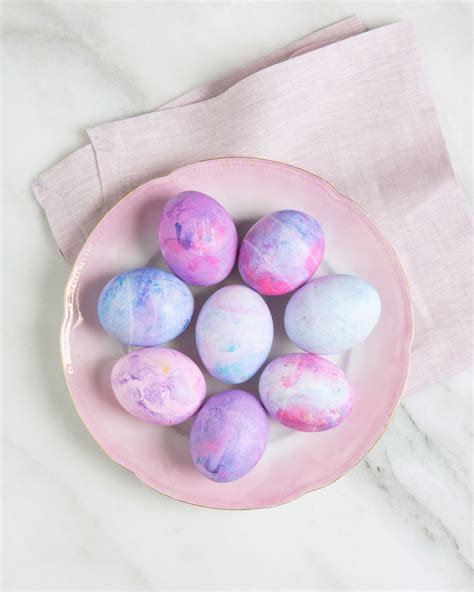 a pink bowl filled with dyed eggs on top of a white marble countertop next to a napkin
