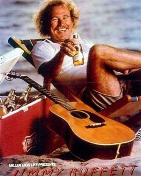 a man sitting on the beach with a guitar and beer in his hand while holding a bottle