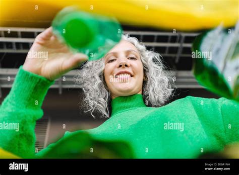 Smiling woman with gray hair putting green bottle in yellow plastic bag Stock Photo - Alamy