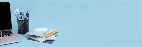 Laptop, stack of notepads, stand with stationery on a blue background. Banner with workspace ...