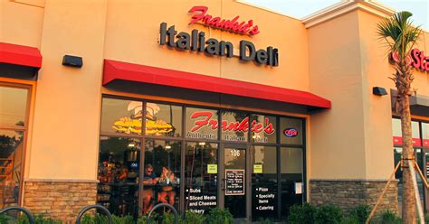 an italian deli restaurant with palm trees in the front and people walking by it