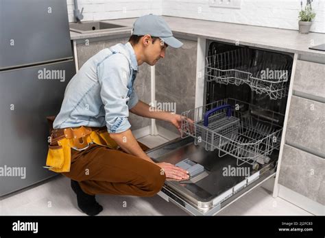 Process of dishwashing machine installation. Young service man setting up dishwasher in new ...