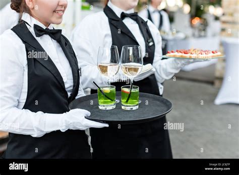 Midsection of professional waiters in uniform serving wine, cocktails and snacks during buffet ...