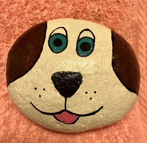 a painted rock with a dog's face and blue eyes on it, sitting on a pink blanket