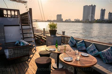 Restaurant on the deck with dining table, sofa, dishware, cutlery on ship in riverside at the ...