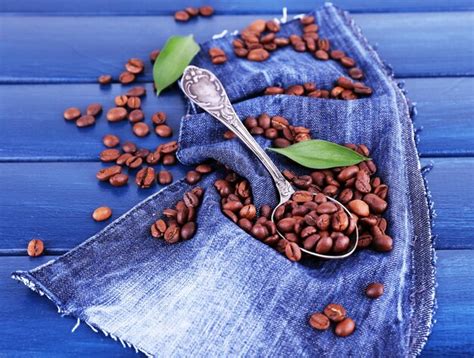 Premium Photo | Green petals near the spoon of coffee beans on blue wooden background with jeans ...