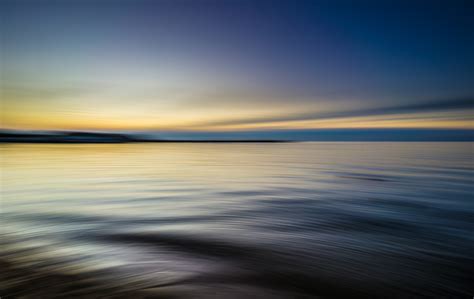 tranquil rippling waters reflect a blue and yellow sky at sunset, water sea calm and horizon 4k ...