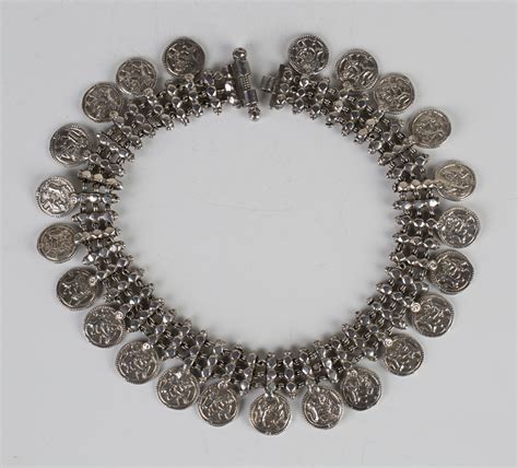 A white metal collar necklace, the front fitted with a row of circular ...