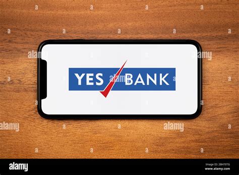 A smartphone showing the Yes Bank logo rests on a plain wooden table ...