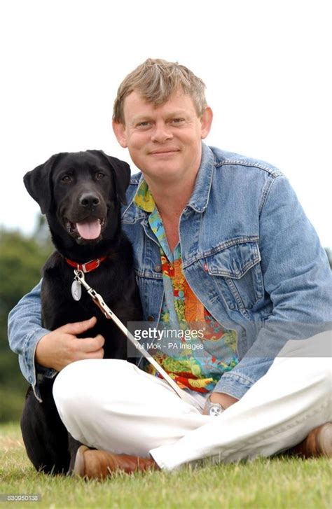 a man sitting on the grass with his dog in front of him and smiling at the camera