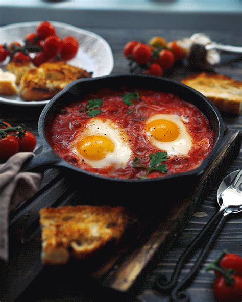 two eggs are in a skillet with tomato sauce and bread on the table next to it