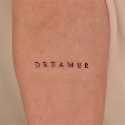 "DREAMER" lettering tattoo on the inner forearm