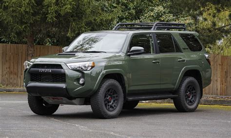 a green toyota 4runner is parked in a parking lot next to a wooden fence