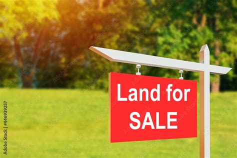 Land for sale sign. Red sign for sale plot. Green lawn behind sign. Land for sale signboard on ...