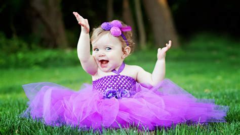 Cute Smiley Girl Baby Is Sitting On Green Grass Wearing Purple Frock And Flower Band On Head ...