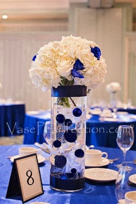 a vase with white and blue flowers is on a table set for an elegant dinner