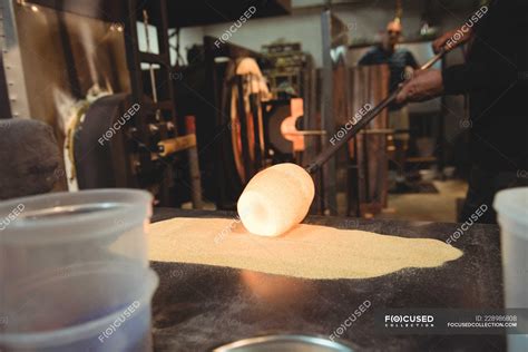 Glassblower rolling molten glass over blowpipe glass on table at glassblowing factory — Men ...